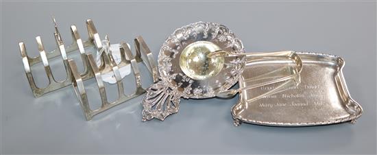 A pair of silver toastracks, a silver presentation dish, a pair of silver sugar tongs and a white metal Hanau strainer.